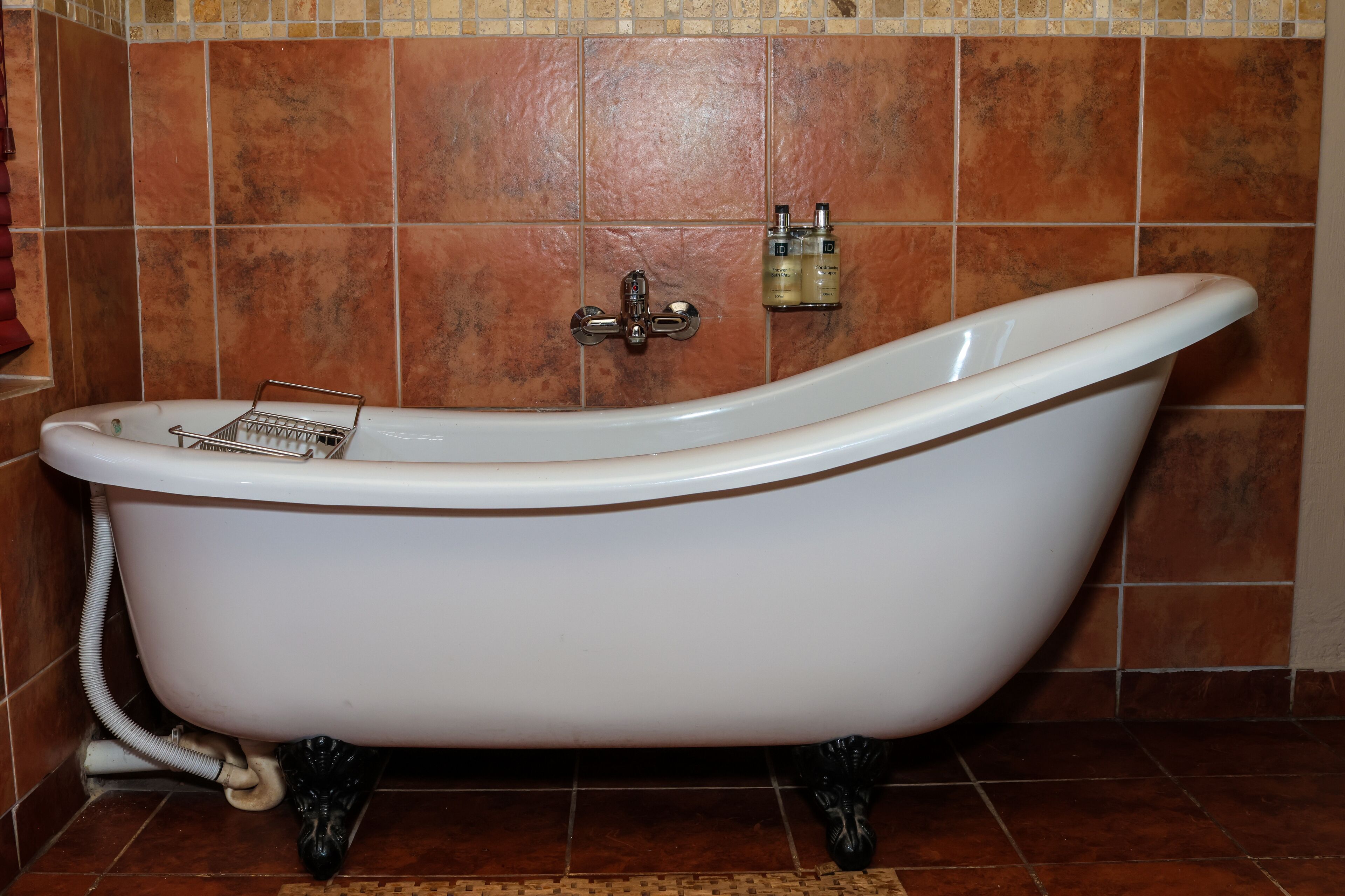 A clawfoot bathtub in a bathroom with brown tiles and a tiled shower area.