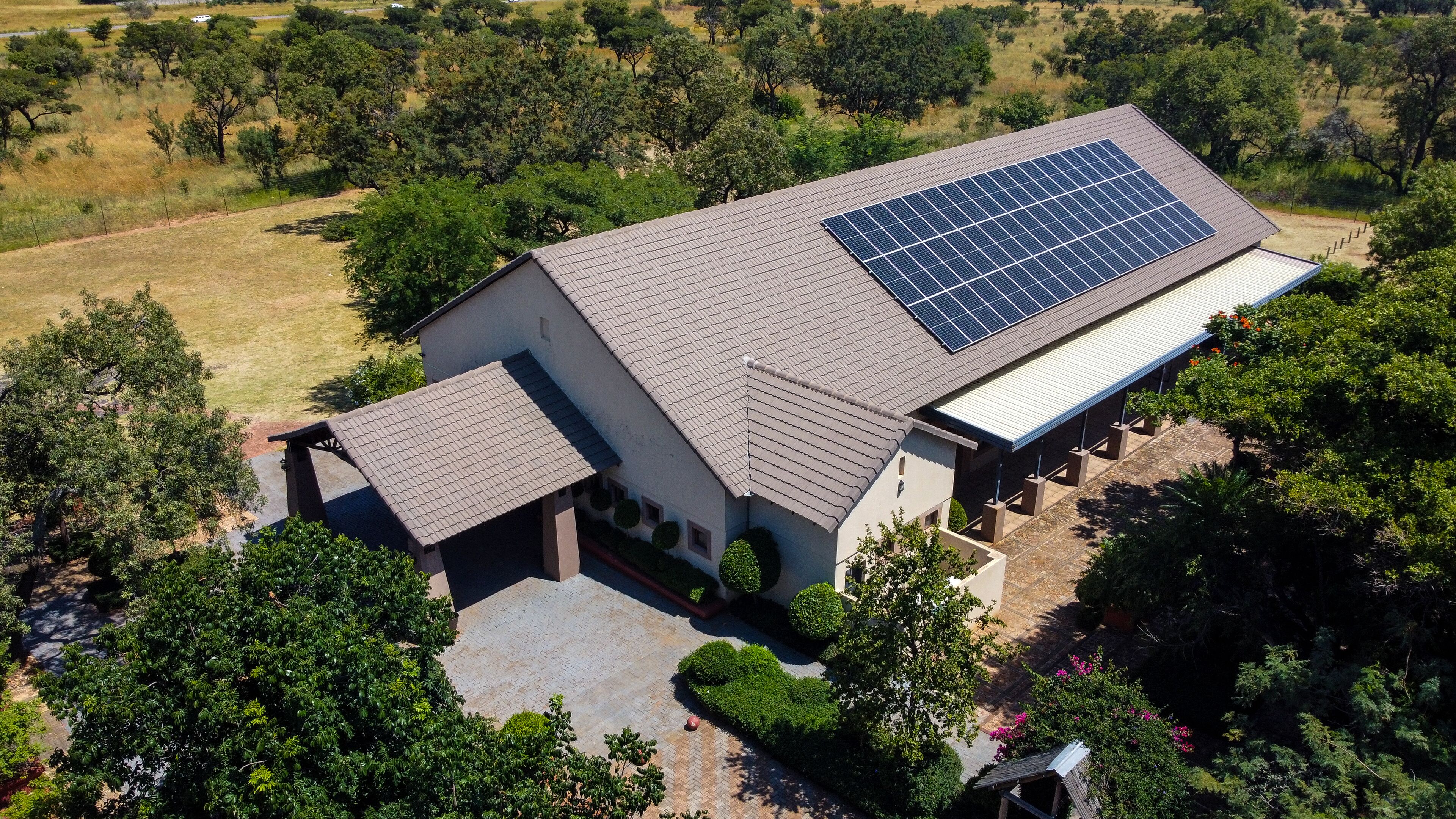 Une maison dotée d’un toit recouvert de panneaux solaires, entourée de verdure et d’arbres.