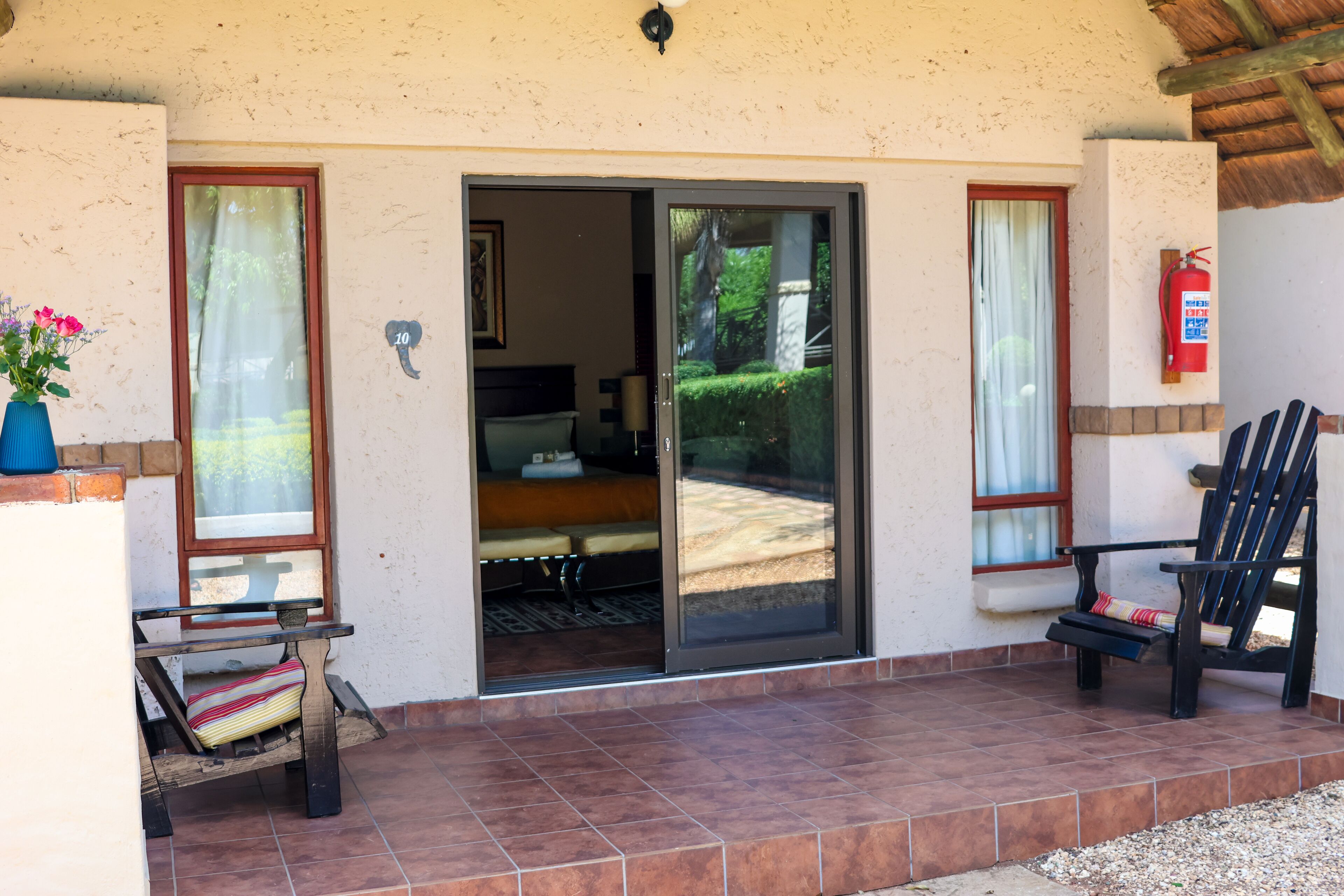 A room with a sliding glass door leading to a balcony, a bed with a striped pillow, a small table, and a chair.