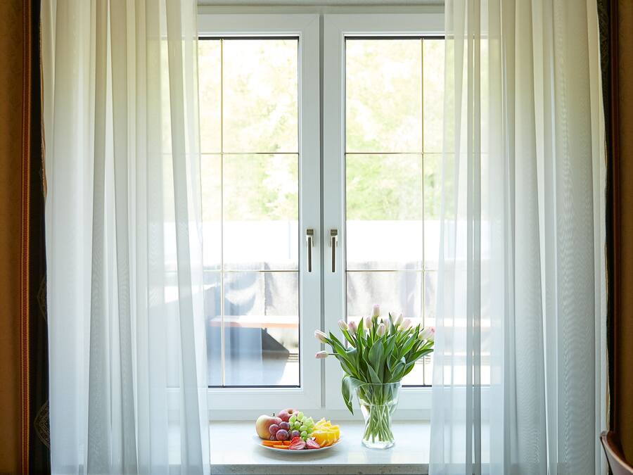 A window with white curtains, a plate of fruit, and a vase of tulips on a windowsill.