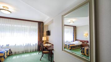 Ein Hotelzimmer mit einem Bett, einem Schreibtisch mit Stuhl, einer Lampe und einem großen Spiegel.