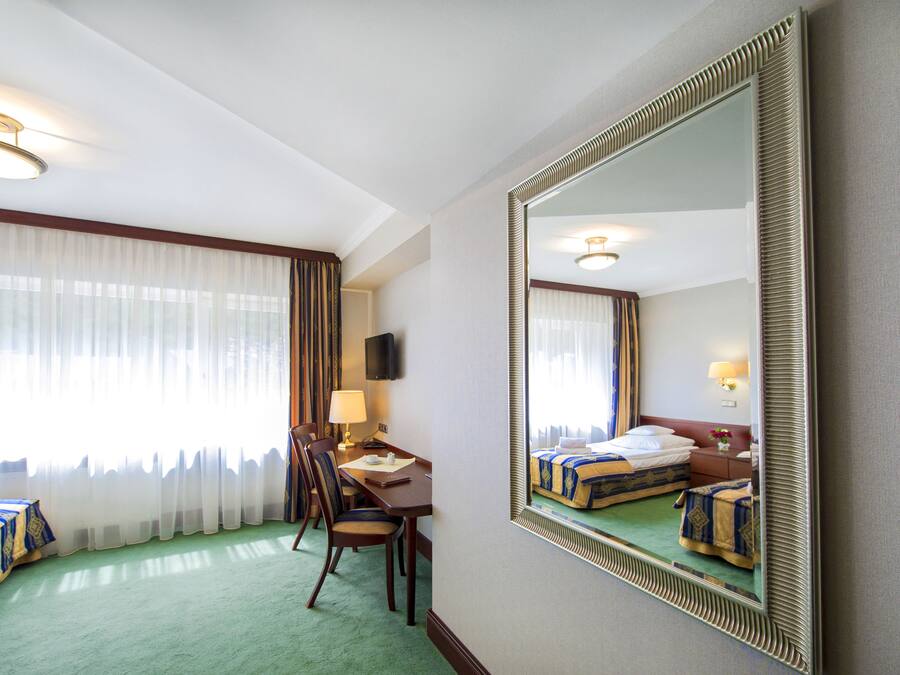 Ein Hotelzimmer mit einem Bett, einem Schreibtisch mit Stuhl, einer Lampe und einem großen Spiegel.