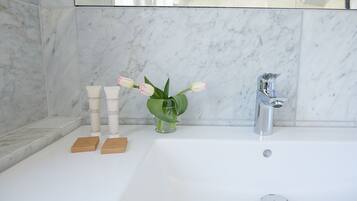 Un baño con pared de mármol, una bañera blanca, un florero de vidrio con flores y dos pequeños cofres de madera.