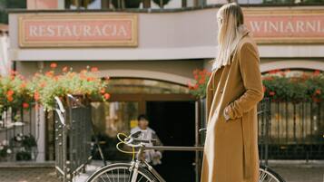 Eine Person steht neben einem Fahrrad vor einem Gebäude, an dem ein Schild mit der Aufschrift "RESTAURACJA WINIARZ" hängt.