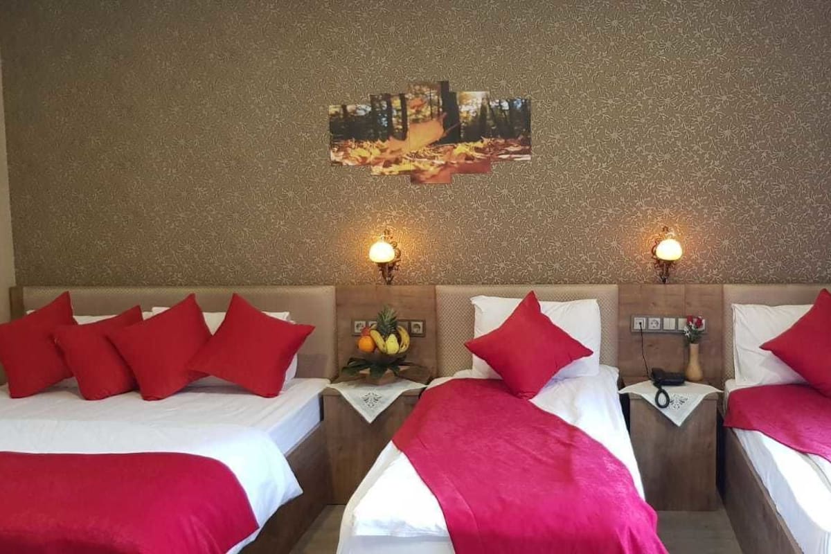 A hotel room with two beds, red pillows, a fruit basket, and a wall-mounted picture.