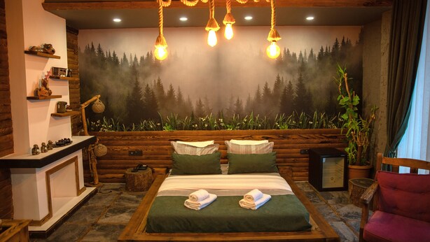 A cozy room with a bed, a wooden bench, a small table, and a wall mural of a forest. - Ayder Hanedan Hotel (Ardesen)