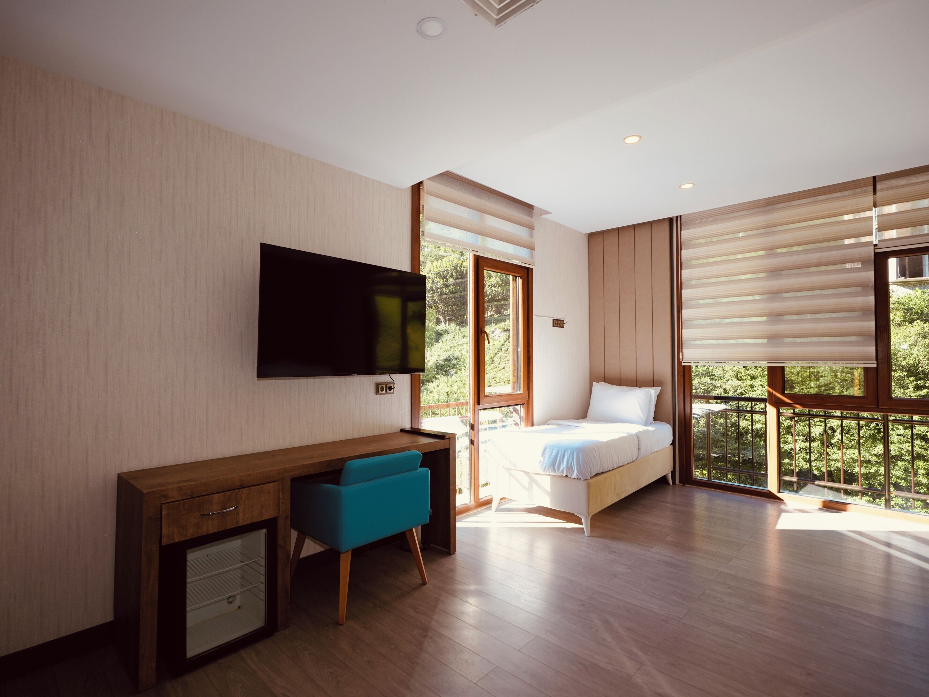 Une chambre à coucher avec un lit, un bureau avec une chaise, une télévision et de grandes fenêtres.