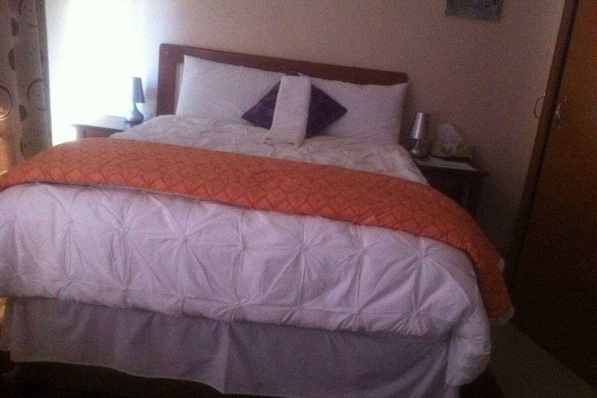 A neatly made bed with a white and orange quilt, a wooden headboard, and a bedside table with a lamp.