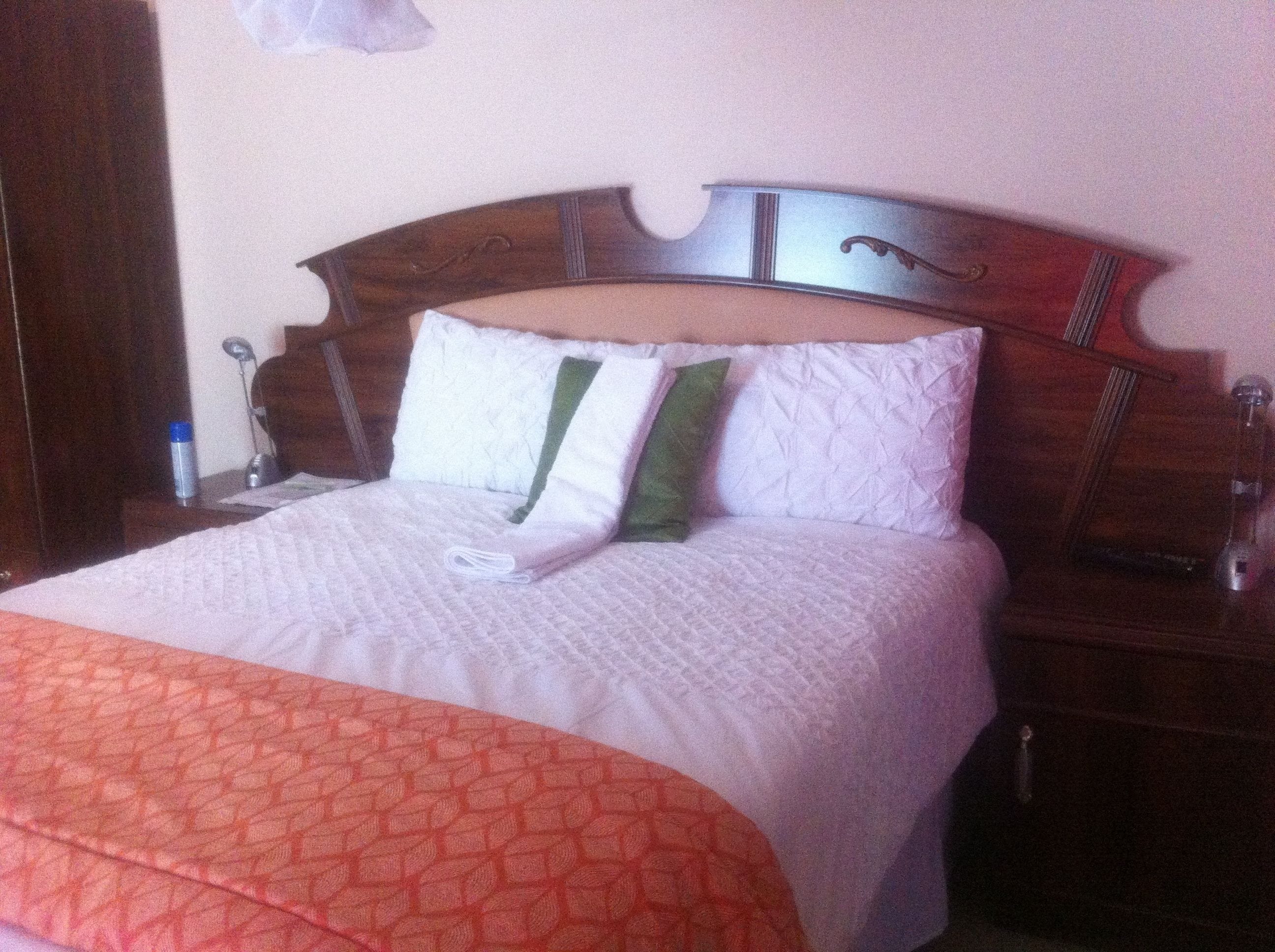 A neatly made bed with a patterned blanket, a wooden headboard, and a bedside table with a lamp and a bottle.