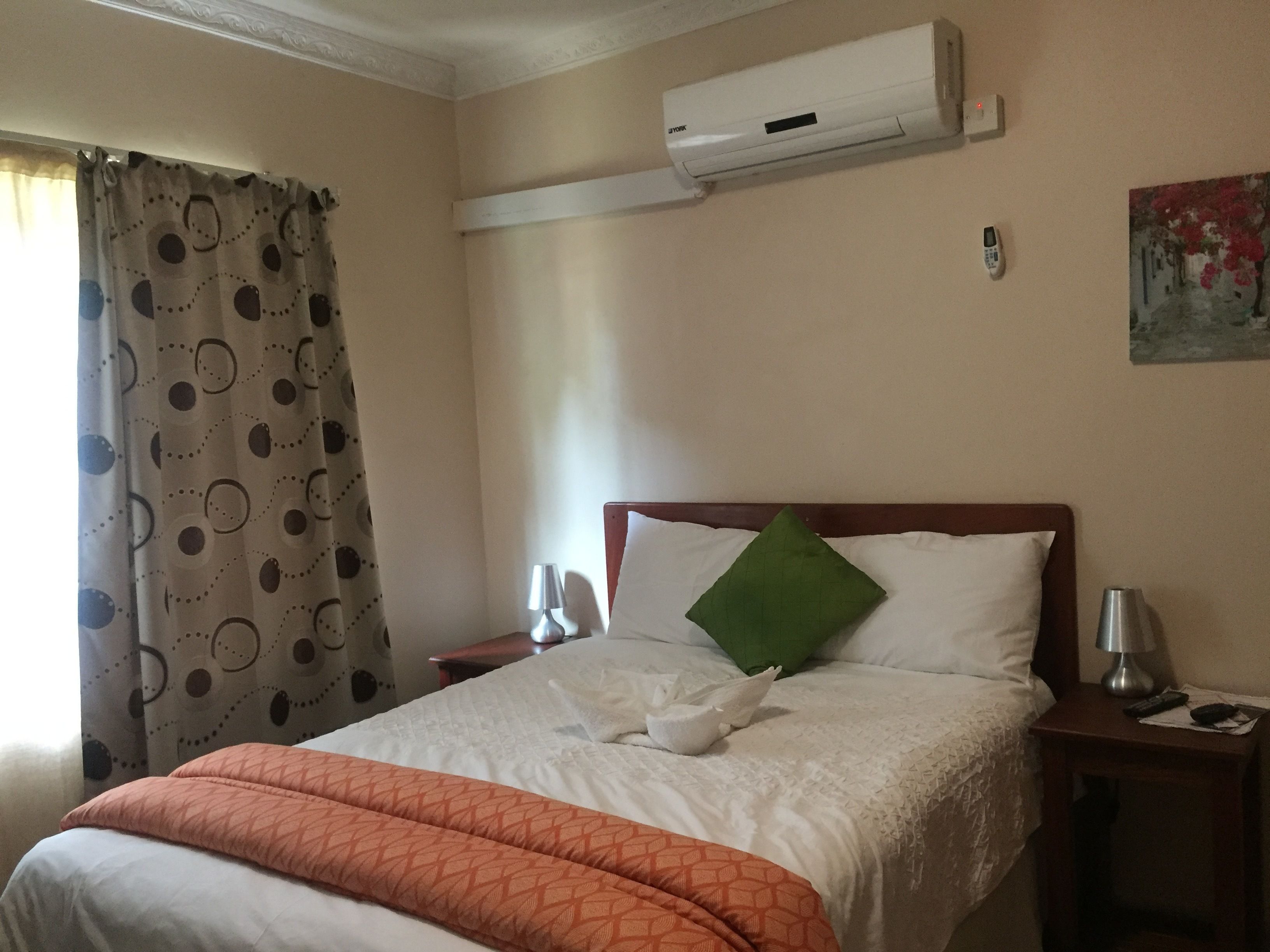 A hotel room with a bed, a nightstand, a lamp, a remote control, and an air conditioning unit on the wall.