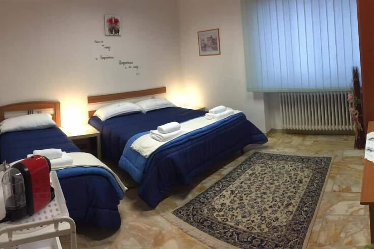 Quarto de hotel com duas camas, uma escrivaninha pequena, um radiador e uma janela com persianas.