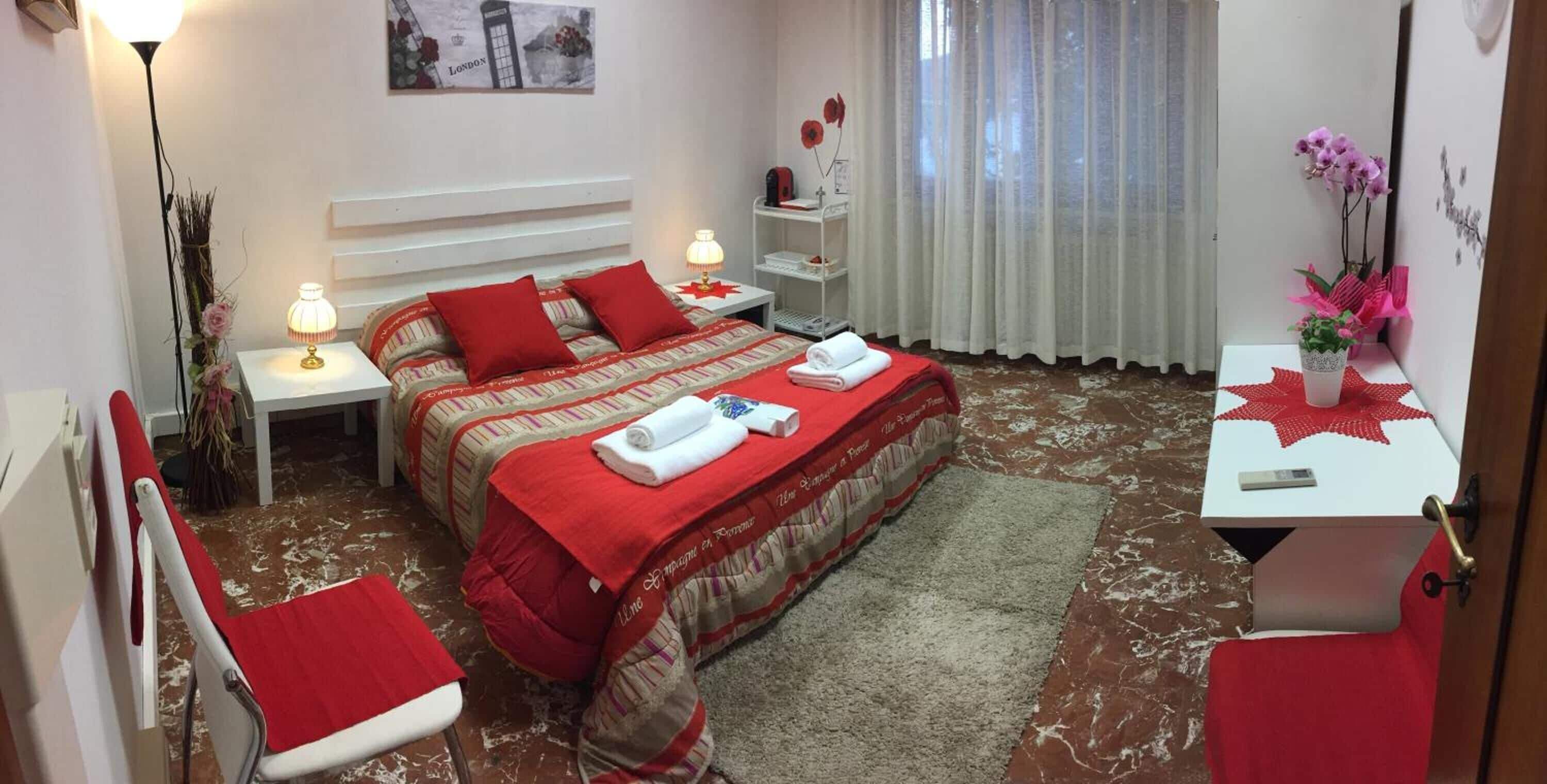 Habitación de hotel con cama, dos mesitas de noche, una silla, un escritorio con teléfono y una ventana con cortinas.