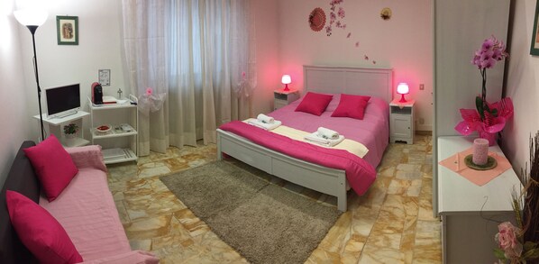Un dormitorio ordenado con cama, mesitas de noche, escritorio, silla y lámpara.