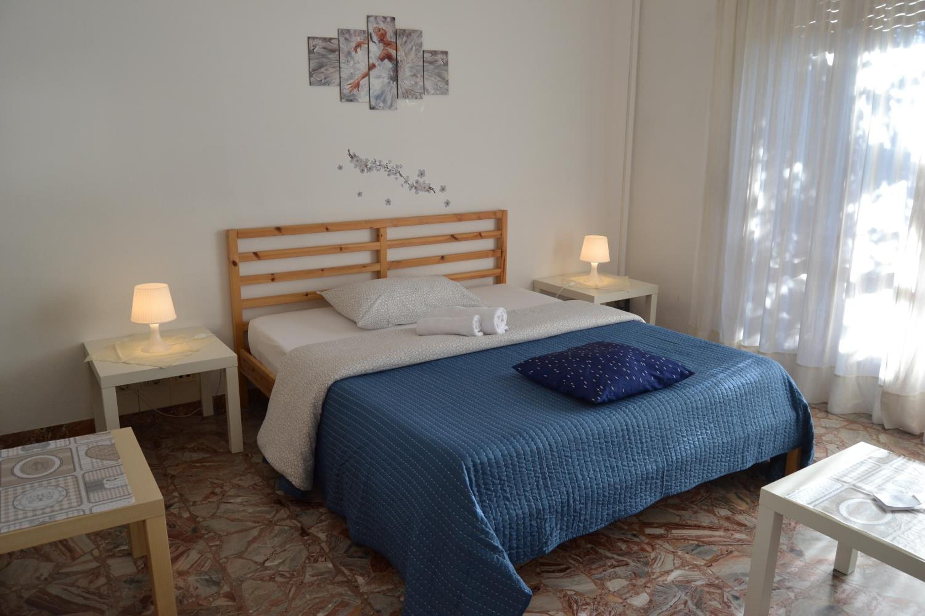 Une chambre à coucher avec une tête de lit en bois, une couvre-lit bleue, deux tables de chevet avec des lampes et un sol à motifs.