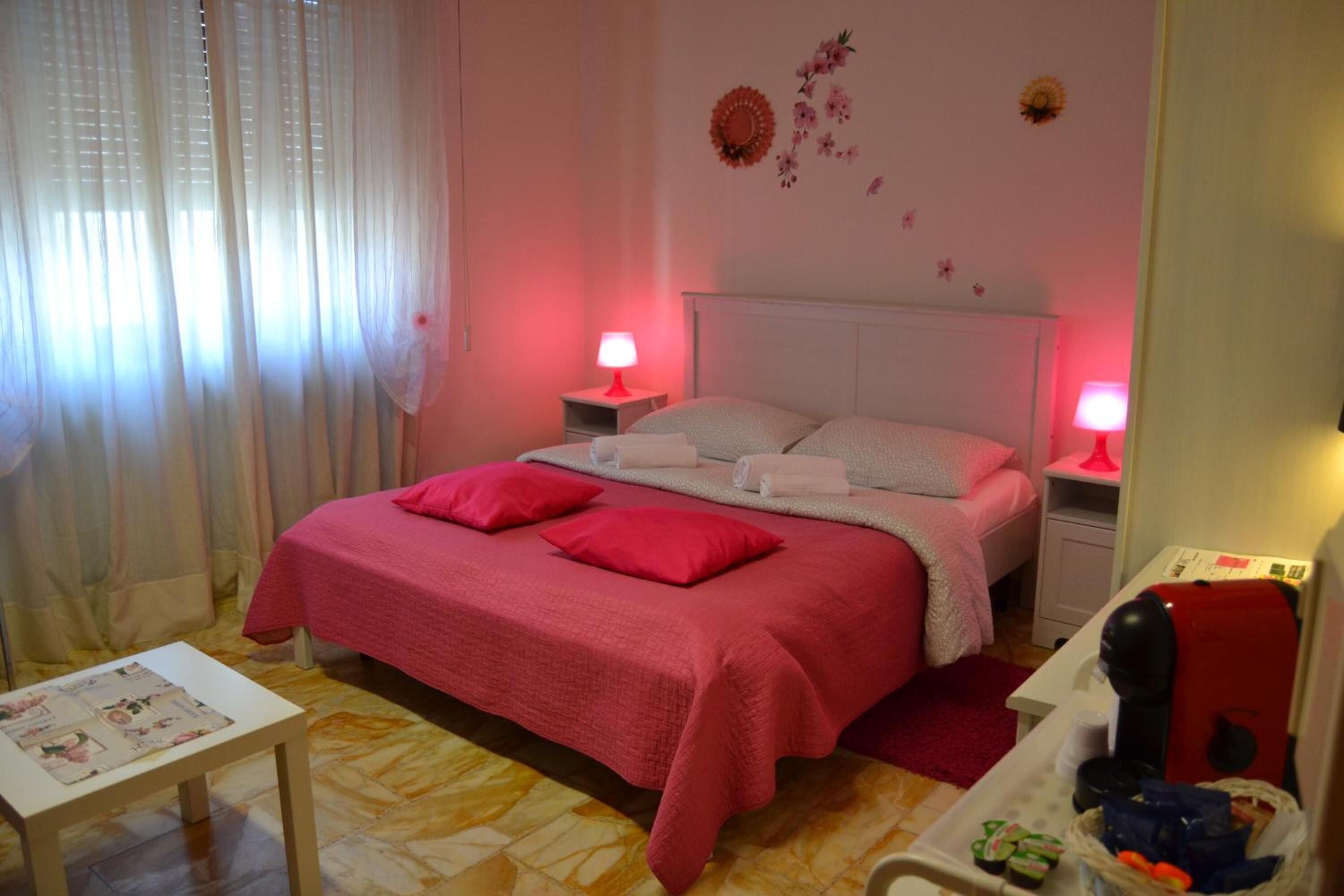 Ein Schlafzimmer mit einem Bett, zwei Nachttischen mit Lampen, einem kleinen Tisch mit Unterlage und einem roten Stuhl.
