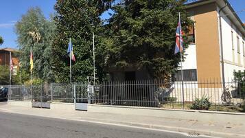 Un edificio con fachada color beige, una cerca metálica y varias banderas.