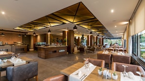 A modern restaurant with wooden tables, leather chairs, and a central bar area. - Vista Hotel (Mezitli)