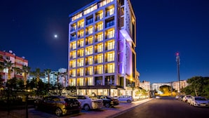A multi-story hotel with a modern design, featuring a prominent entrance and a parking area with several cars. - Vista Hotel (Mezitli)