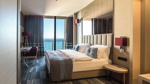 A modern hotel room with a large bed, a desk, and a view of the sea. - Vista Hotel (Mezitli)