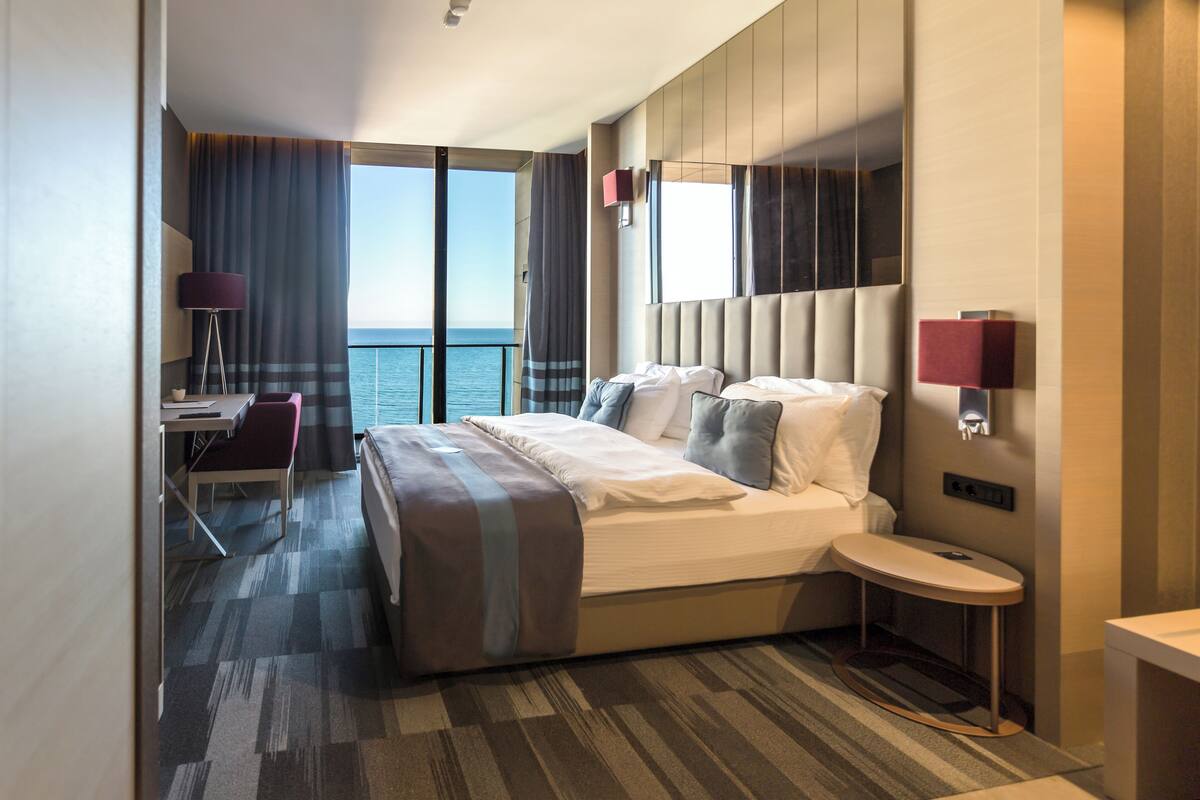 Ein modernes Hotelzimmer mit einem großen Bett, einem Schreibtisch und Blick auf das Meer.