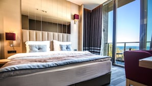 A modern hotel room with a large bed, a desk, and a view of the sea. - Vista Hotel (Mezitli)