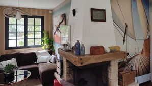 Een gezellige woonkamer met een open haard, een groot raam en een muurschildering met een nautisch thema.