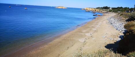 A beach with clear blue water, a rocky shoreline, and a distant rocky outcrop.