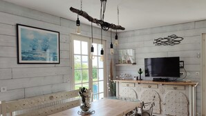 Een eethoek met een houten tafel en metalen stoelen, een televisie op een houten dressoir, en een schilderij aan de muur.
