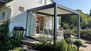 Een huis met een overdekte patio, een zichtbare deur en een tuin met verschillende planten en bloemen.