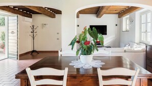 A dining area with a wooden table, white chairs, and a potted plant with red flowers. - Luxury Tuscany Villa with Private Pool, 13 Sleeps. Lucca 10 km. (San Ginese Di Compito Lucca)