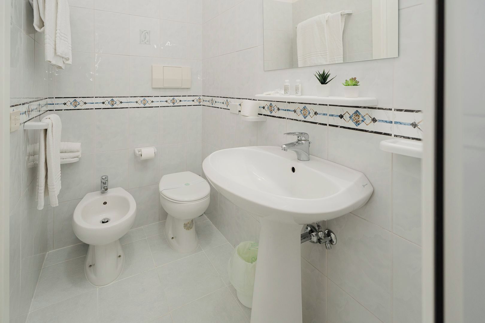 Un baño con bidé, inodoro y lavamanos, todo en color blanco.