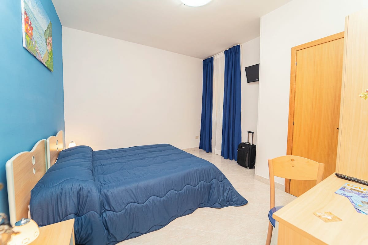 A bedroom with a bed, a desk, a chair, a TV, and a door.