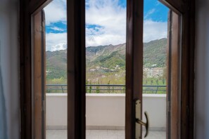 A view from a balcony with a wooden door, overlooking a mountainous landscape with scattered buildings.