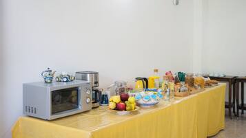Una mesa con mantel amarillo presenta una barra de desayuno con microondas, cafetera y diversos alimentos.