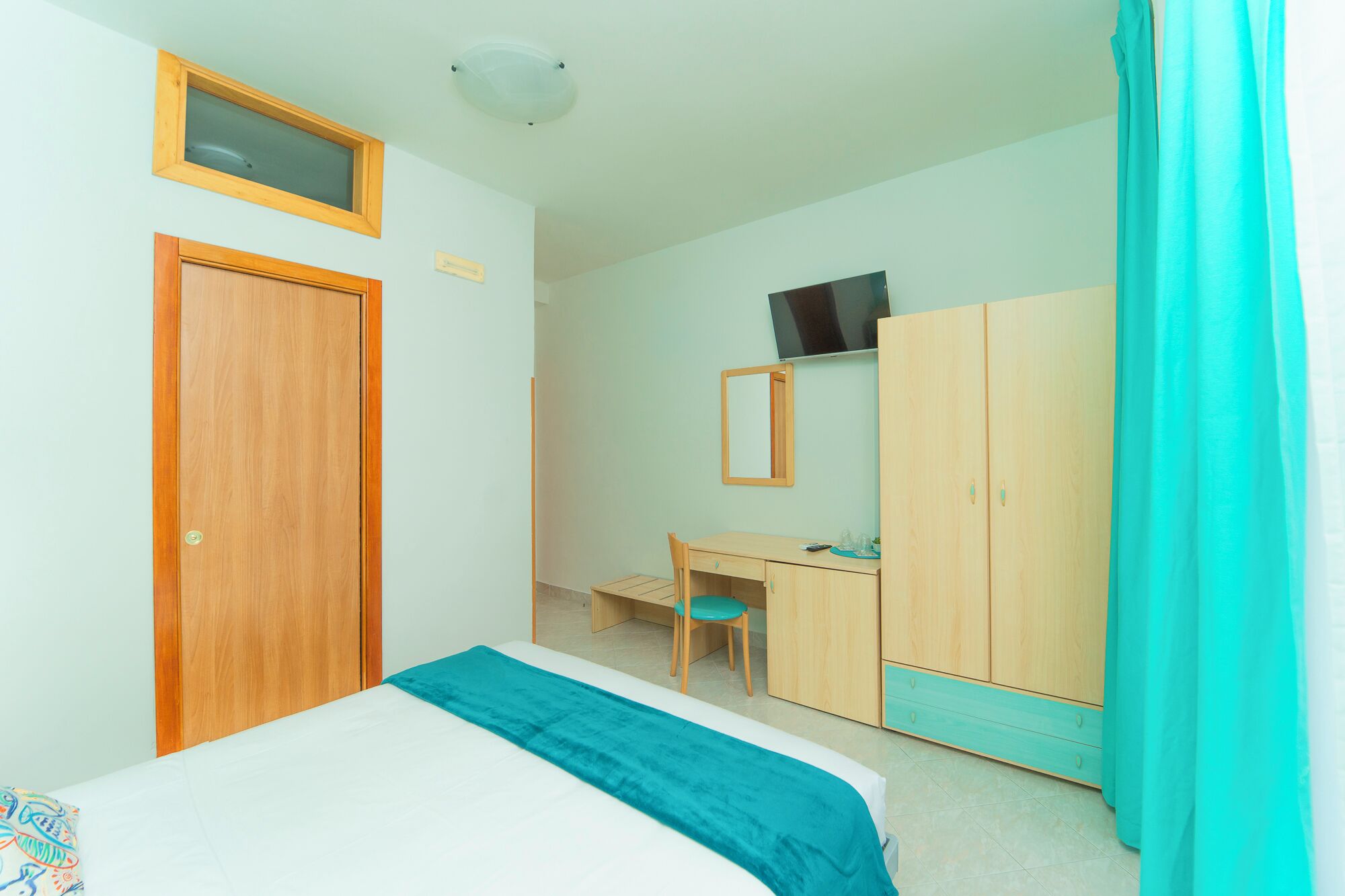 Un dormitorio con cama, escritorio, silla, armario y televisor en la pared.
