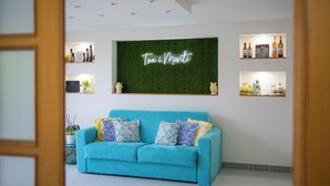 A modern living room with a teal sofa, decorative pillows, a green wall with a neon sign, and shelves with bottles and decorative items. - Tra i Monti (Tramonti)