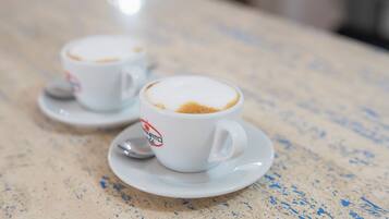 Zwei weiße Kaffeetassen mit einem Logo auf dem Untersetzer, auf einer fleckigen Arbeitsplatte platziert.