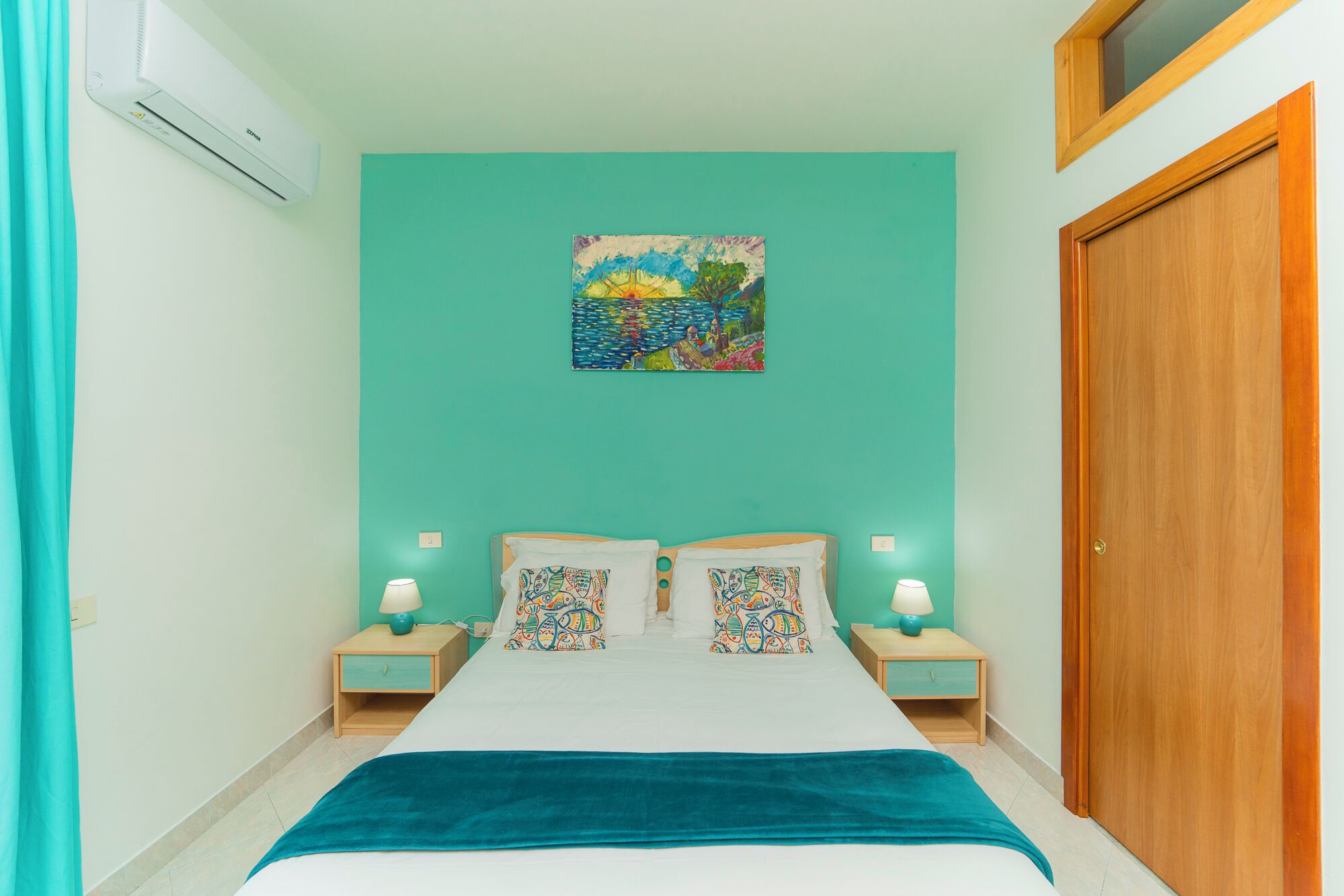 Una camera da letto con un letto, due comodini con lampade, una parete color acquamarina, una porta in legno e un quadro sopra il letto.
