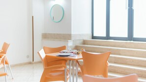 A dining area with orange chairs and a table set for two, a mirror on the wall, and a staircase leading to an upper level. - Tra i Monti (Tramonti)