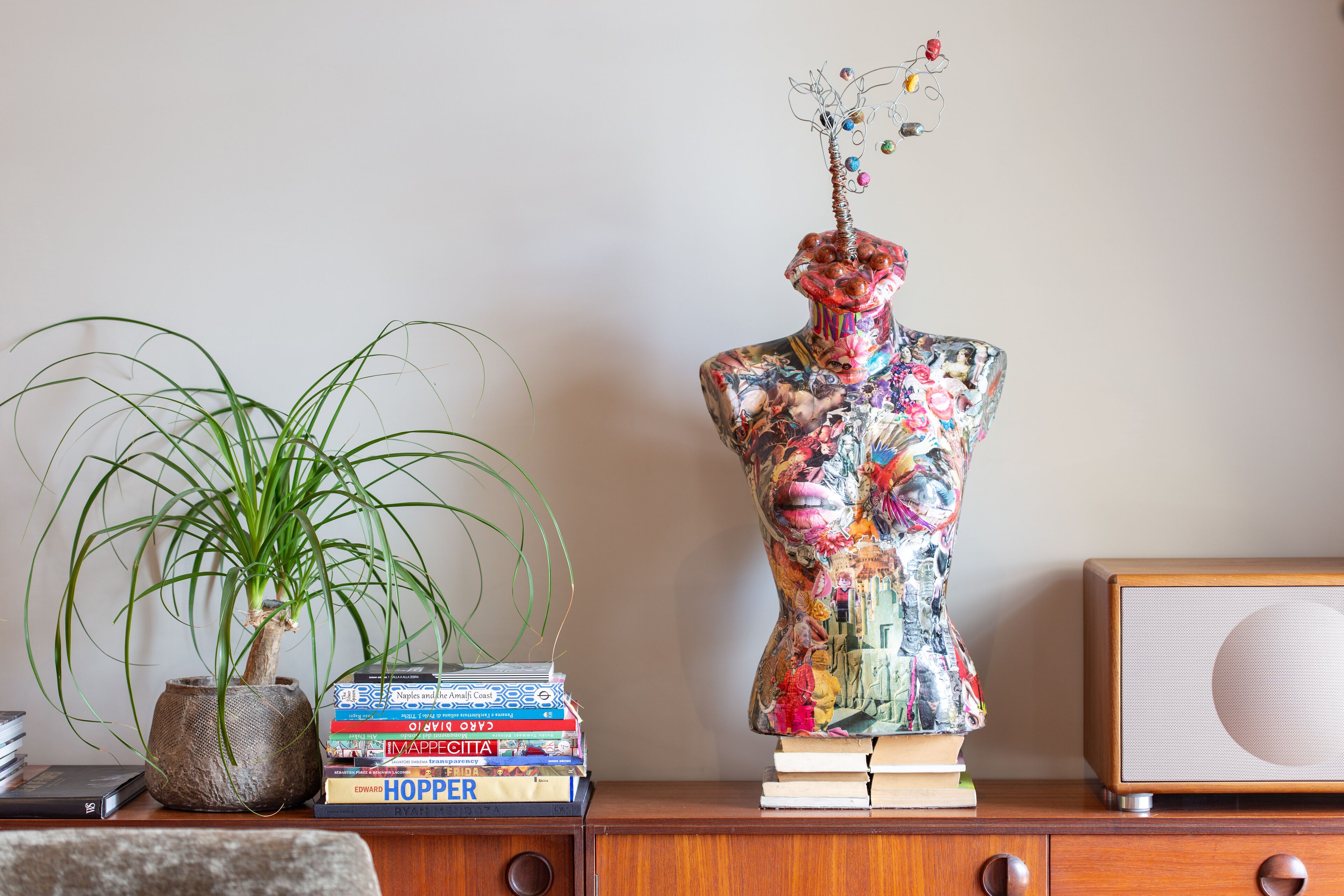 Une commode en bois ornée d’un vase, d’une pile de livres, d’une plante en pot et d’une sculpture décorative.