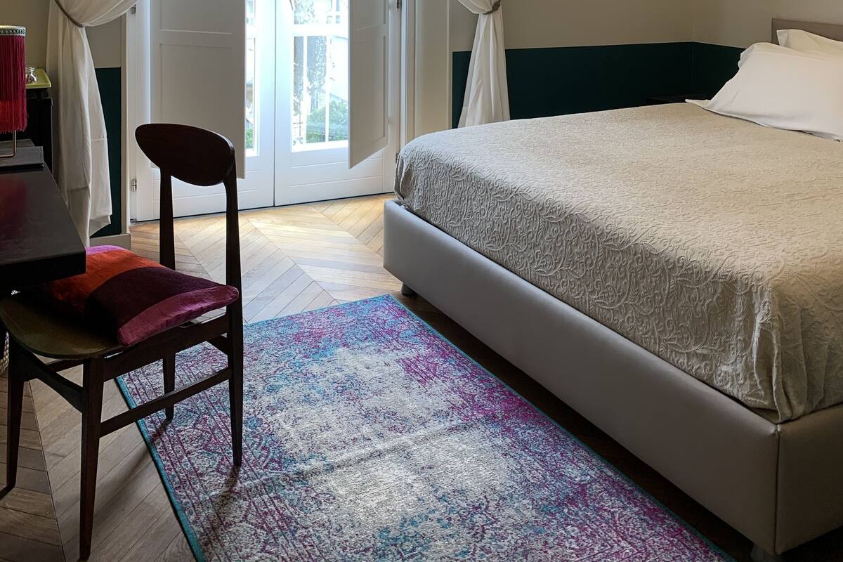 Ein Schlafzimmer mit einem Bett, einem Sessel, einem Schreibtisch und einem Fenster mit Vorhängen.