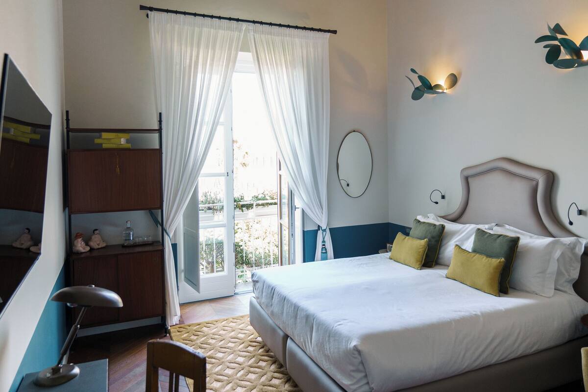 Ein Schlafzimmer mit Bett, Schreibtisch, Stuhl, Fernseher und einem Fenster mit Vorhängen.