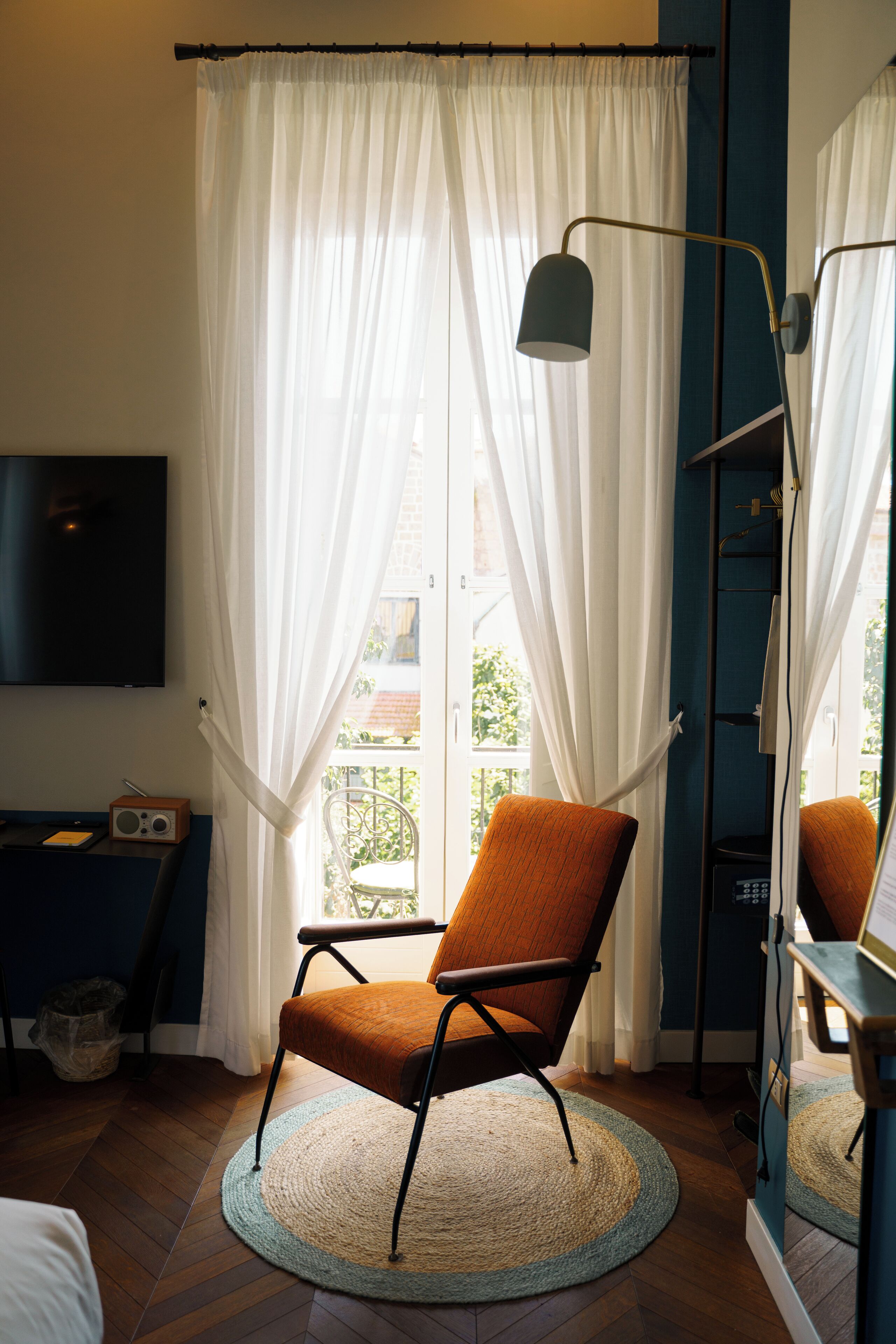 A room with a TV mounted on the wall, a chair with a woven rug, and a window with sheer curtains.