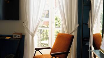 A room with a TV mounted on the wall, a chair with a woven rug, and a window with sheer curtains.