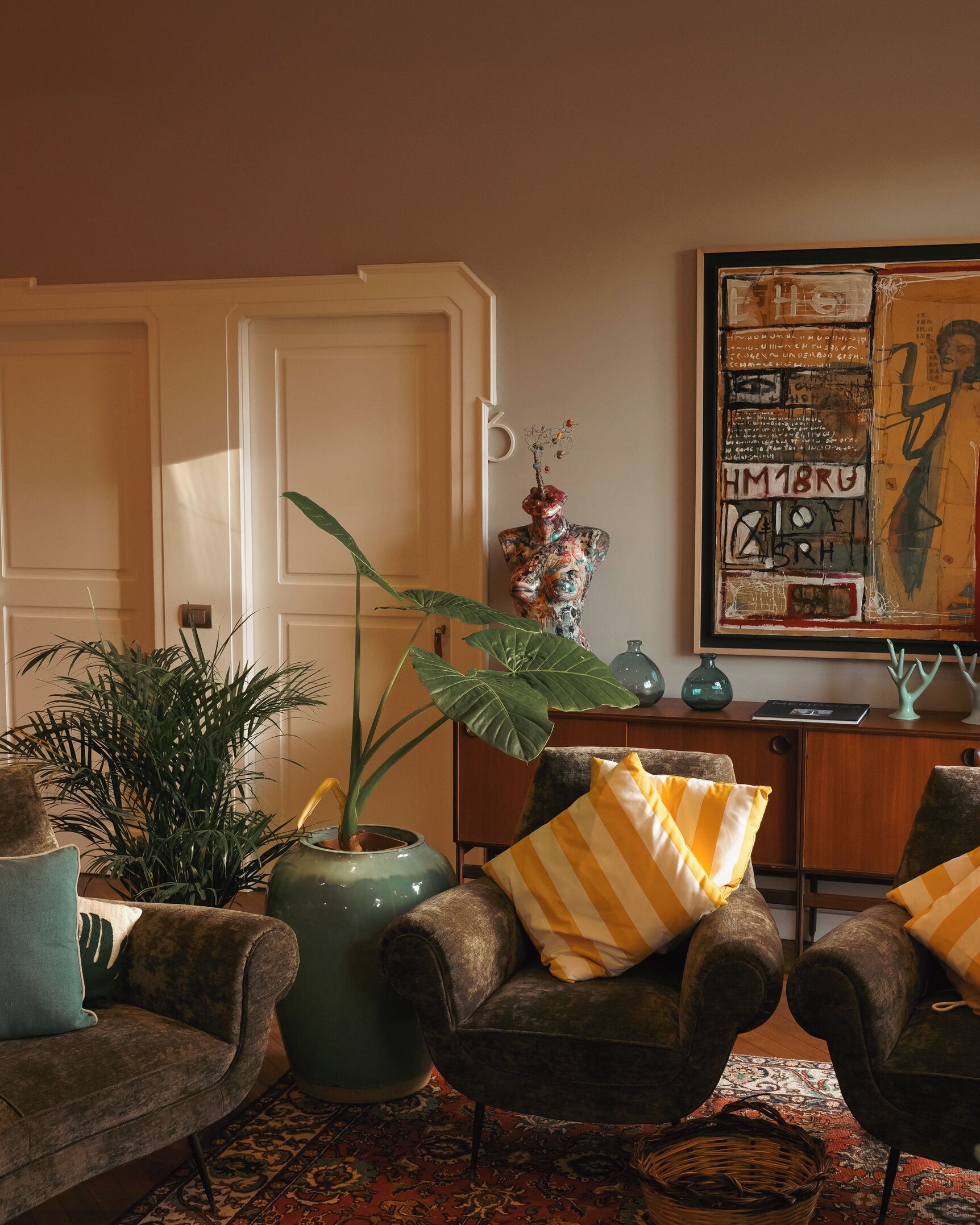 Un salon chaleureux avec une grande plante verte, deux fauteuils dotés de coussins à rayures, un tapis à motifs et un vase décoratif.