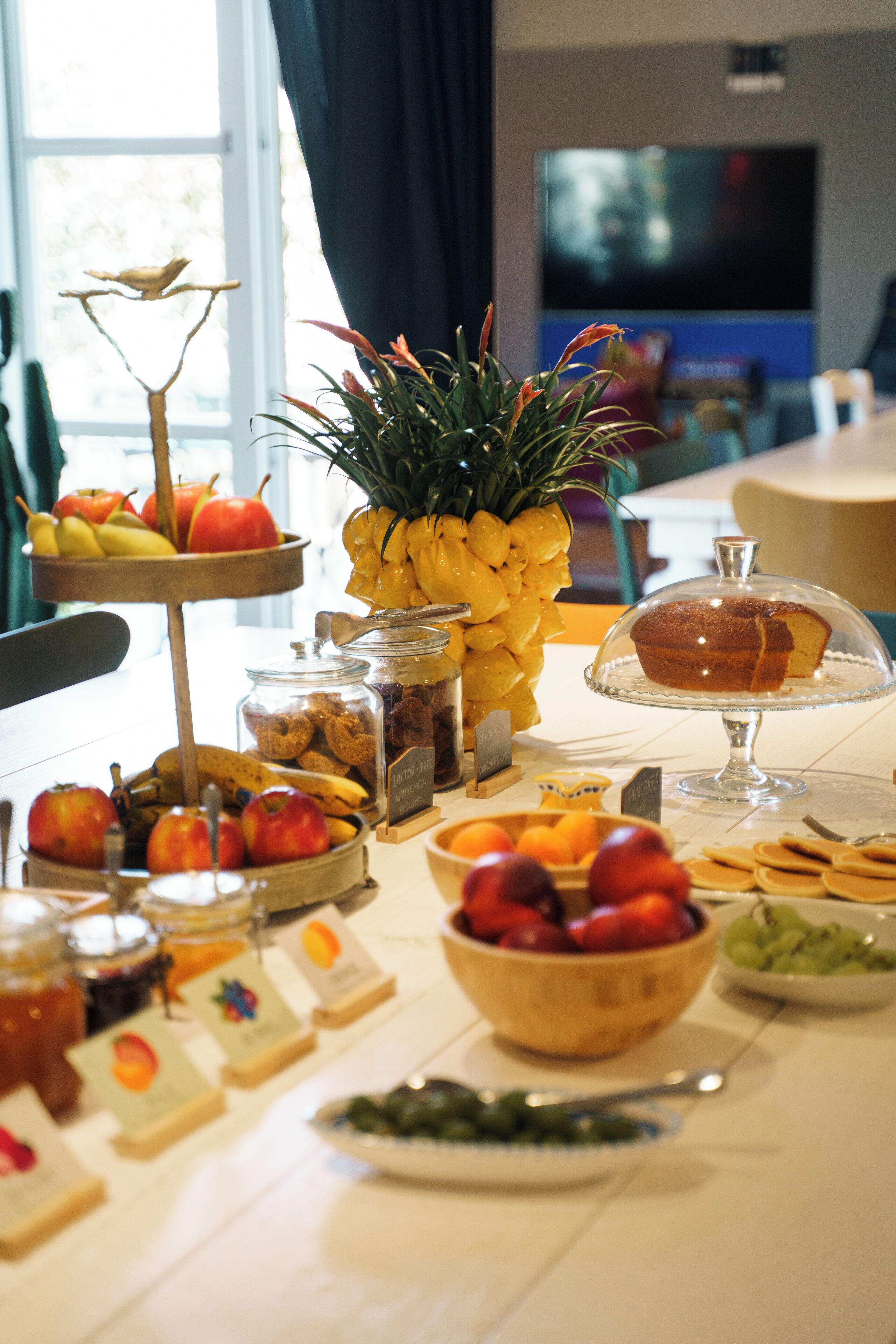 A buffet table with various fruits, a pineapple centerpiece, and a cake on a glass stand.