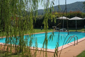 Piscina com espreguiçadeiras e guarda-sóis, cercada por vegetação e colinas.