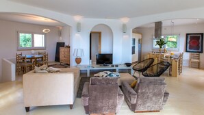 A spacious living area with a sofa, armchairs, a TV, and a dining area with a table and chairs.