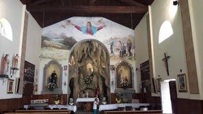 A church interior with a large mural, altar, and religious statues.
