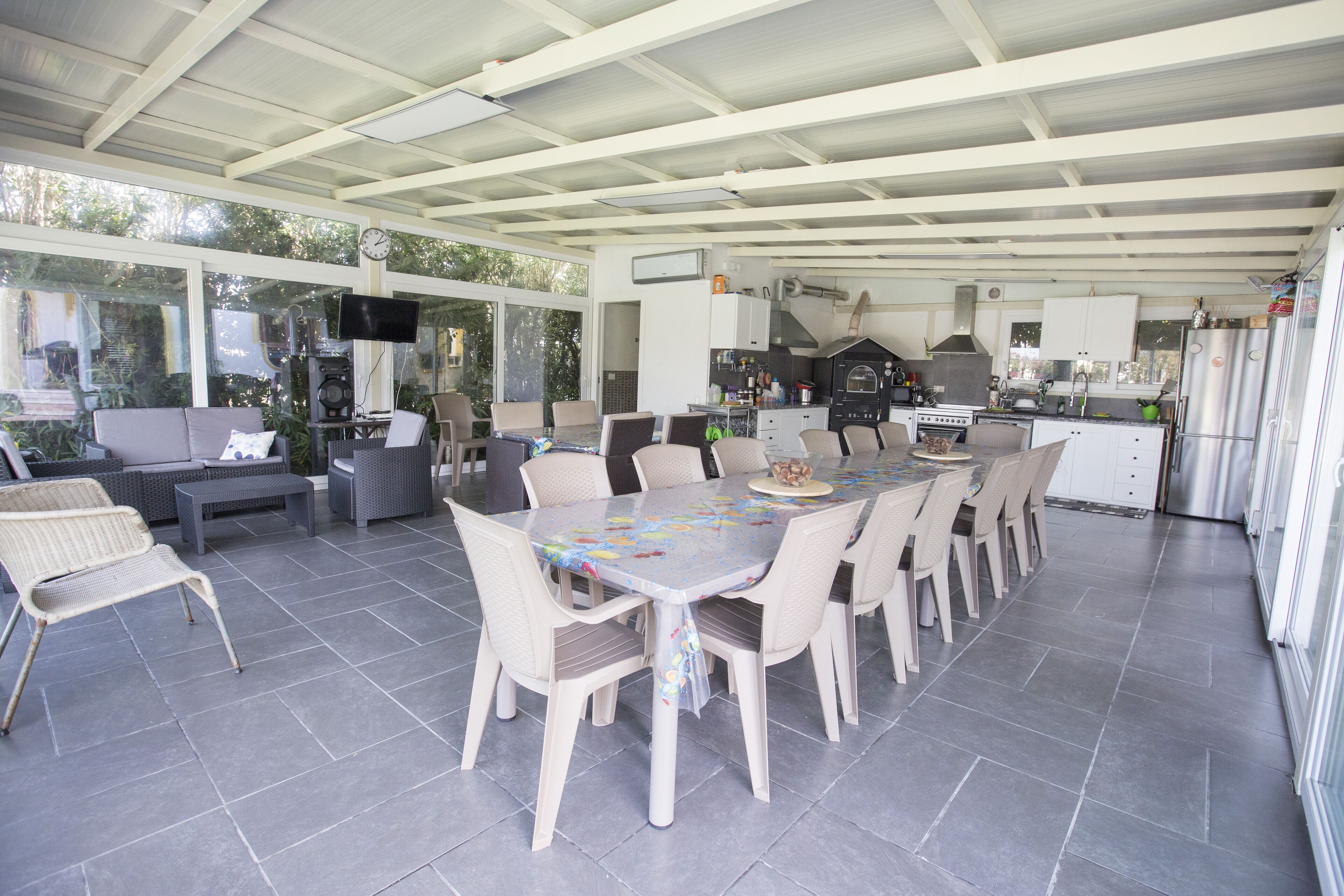 Un espace extérieur abrité, aménagé pour les repas, avec une grande table et des chaises, un canapé et un coin cuisine équipé d’appareils électroménagers.